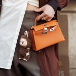 PARIS, FRANCE - MARCH 08: A guest wears brown coat, white blouse, orange Hermes bag with a bag charm brown Labubu monster, grey pants outside the Hermes fashion show during the Womenswear Fall/Winter 2025/2026 as part of Paris Fashion Week on March 08, 2025 in Paris, France. (Photo by Raimonda Kulikauskiene/Getty Images)
